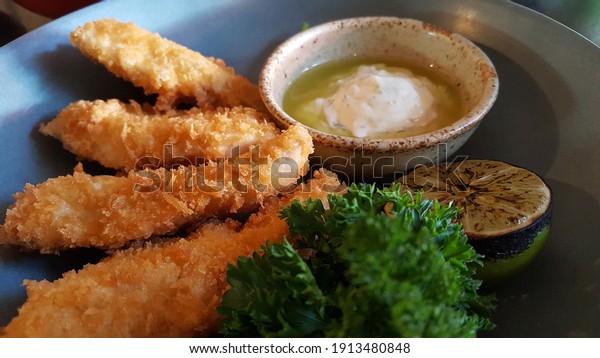 View of crispy fish steak, fish fingers or\
strips served with home-maded tar tar sauce with olive oil.  Kid\
meal, appertiser or snack food made using a whitefish (cod, hake,\
haddock or pollock)