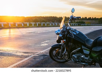 view of a cruise motorcycle, chopper class, parked by an asphalt road, highway against the background of the setting sun