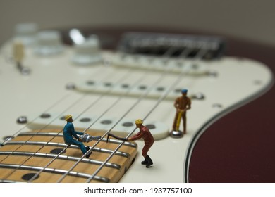 A View Of A Cutout Of An Electric Guitar Where Miniature Figures Work With A Chainsaw And Line Up Hammer. Close Up View