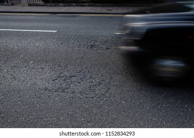 A view of a damaged and worn road surface with an unrecognisable blurred car travelling over the road
