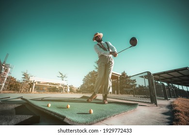 View of a dapper adult black guy with a beard and a cigar, in a hat and elegant trousers with suspenders, he is warming up and practicing before the golf play on the field, sunny day, teal sky