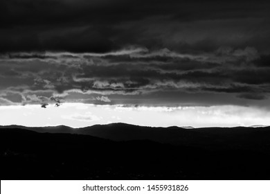 View of dark clouds at sunset, with sun filtering through an hole over the mountains