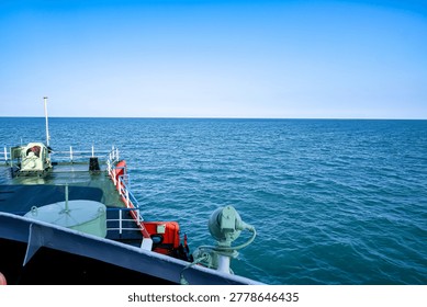 View from the deck of a ferry ship sailing on the calm blue ocean under a clear sky. Industrial maritime vessel details with a vast horizon of deep blue sea water background.