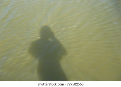 View from the deck of a sailboat looking down at green water.  The shadow of the boat and the photographer (sailor) can be seen.