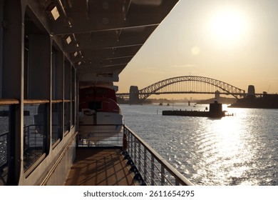 A view from the deck of a ship looking out towards the Sydney Harbour Bridge at what appears to be sunrise or sunset.
