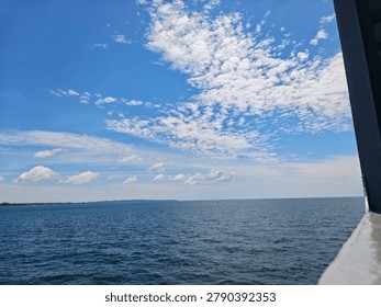 View of the deep blue ocean and distant land under a bright sky with scattered altocumulus clouds.