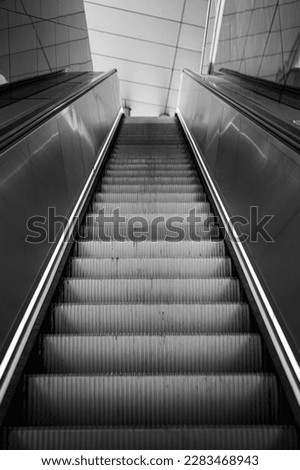 The view from a deep position over a modern stainless steel escalator without people in monochrome.