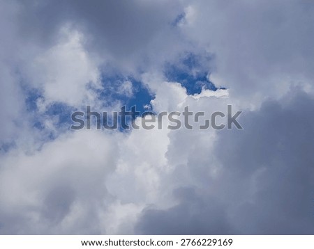 View of dense storm clouds with a small opening of blue sky creating a dramatic contrast between dark and light areas. Perfect for weather concepts, climate visuals, atmospheric backgrounds, and mood transition themes.