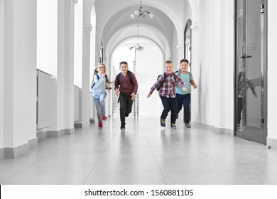 View from distance of three boys and one blonde girl playing together and running on long white school corridor. Pupils going home after hard day and lessons, feeling happy.