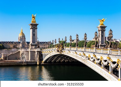 View of the Dome des Invalides from the Pont Alexandre III bridge in the summer morning. Pont Alexandre III bridge decorated with ornate Art Nouveau lamps and sculptures.