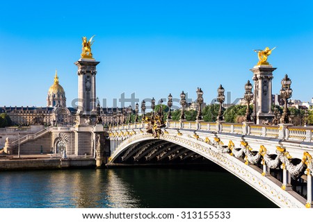 View of the Dome des Invalides from the Pont Alexandre III bridge in the summer morning. Pont Alexandre III bridge decorated with ornate Art Nouveau lamps and sculptures.