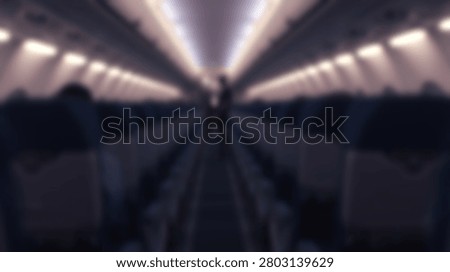 A view down the aisle of an empty airplane cabin, showing rows of dark seats and illuminated overhead lights creating a sense of perspective.