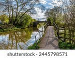 A view down the canal path towards a footbridge over the Grand Union Canal in Aylestone Meadows, Leicester, UK in Springtime