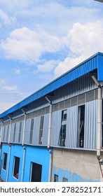 View down a corridor between two blue industrial warehouse buildings with a cloudy sky