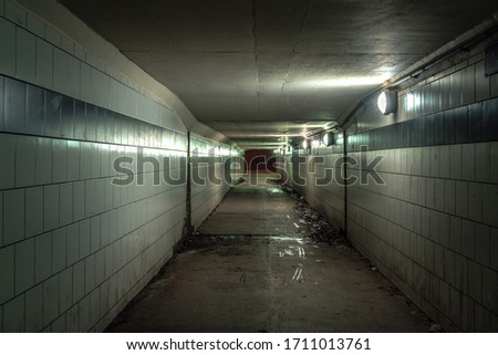 A view down a damp and dirty glazed tiled block and concrete tunnel urban or city pedestrian underpass corridor below Lake Shore Drive in Chicago with white and blue colors and lights on the wall.