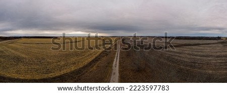 View down a dirt road through with bleak looking harvest farm fields under a grey sky

