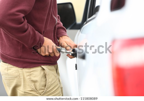 View\
down the length of a car to a man committting a car break in and\
theft with a screw driver inserted into the\
lock
