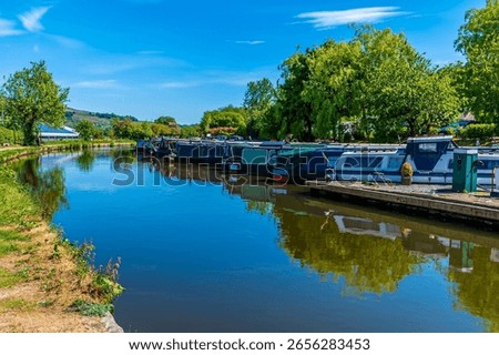 A  view down the Peak Forest Canal past moored canal barges at New Mills, High Peak in the UK in summertime