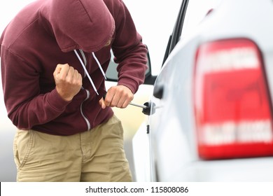View down the side of a car to a man in a hooded top breaking into a car with a screwdriver in order to steal it