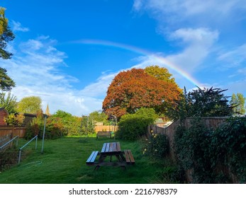 View Down A UK Back Garden In Autumn With A Rainbow Arching Across The Sky