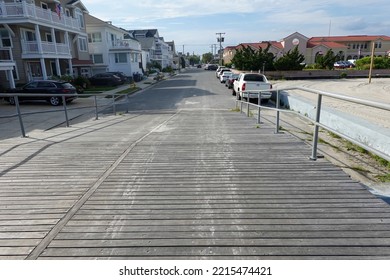 View Down A Wooden Plank Boardwalk Ramp To An Asphalt Street In A Beach Town