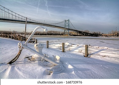 A view of downtown Toledo Ohio's High Level suspension bridge as it crosses over the frozen Maumme river.  An old ship anchor is seen in the snow in the foreground. 