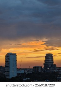 A view of dramatic bright orange sunset with heavy grey clouds over high rise buildings in south west London 
