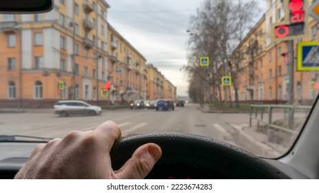 view of the driver hand inside the car, waiting for the traffic light at the intersection of city streets, giving way to other cars