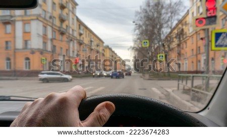 view of the driver hand inside the car, waiting for the traffic light at the intersection of city streets, giving way to other cars