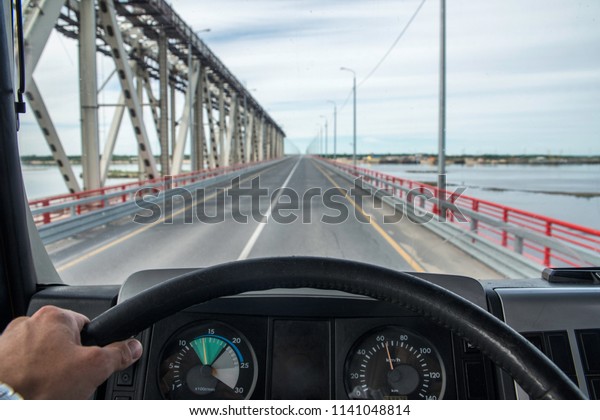 A view from the driver\'s cab of a truck\
moving along an asphalt summer\
road.