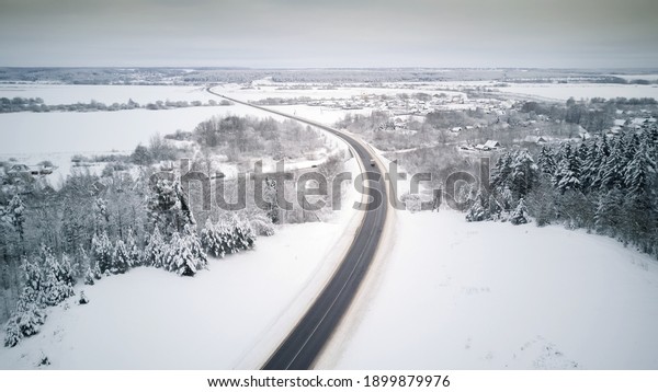View\
from the drone on the paved road, cars, winter snow-covered forest,\
village. Beautiful winter landscape with paved\
road
