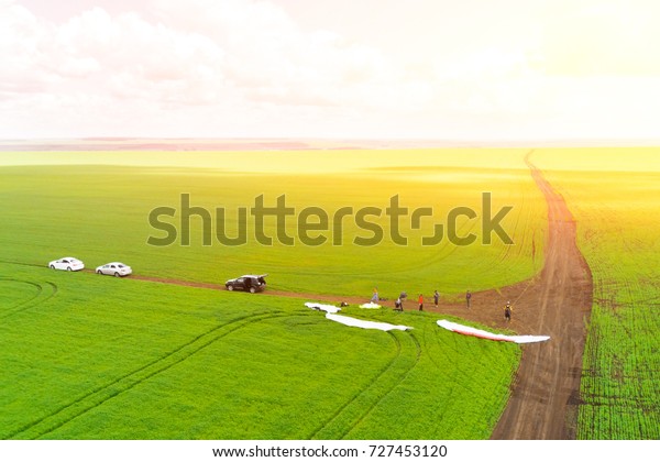 View from the drone\
of the people on the green field are preparing for a flight on\
paraplanes in the sunlight