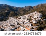 View from drone of picturesque Spanish town of Ojen in green valley surrounded by Sierra Blanca and Sierra Alpujata mountan ranges on sunny fall day, Malaga province