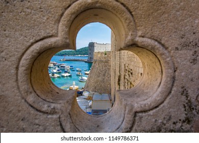 View Of Dubrovnik On Old City, Stone Walls, Sea And Boats With Yachts Through Lucky Clover Trefoil - Ornaments In Gothic Architecture Is Quatrefoil On Bridge At Exit Of Ploce Gate, Dalamtia, Croatia