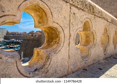 View Of Dubrovnik On Old City, Stone Walls, Sea And Boats With Yachts Through Lucky Clover Trefoil - Ornaments In Gothic Architecture Is Quatrefoil On Bridge At Exit Of Ploce Gate, Dalamtia, Croatia