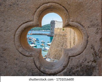 View Of Dubrovnik On Old City, Stone Walls, Sea And Boats With Yachts Through Lucky Clover Trefoil - Ornaments In Gothic Architecture Is Quatrefoil On Bridge At Exit Of Ploce Gate, Dalamtia, Croatia