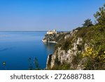 View of Duino Castle seen through blooming spring bushes along the Rilke Trail, a scenic tourist path overlooking the Gulf of Trieste, Friuli Venezia Giulia, Italy.
