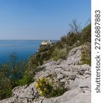 View of Duino Castle seen through blooming spring bushes along the Rilke Trail, a scenic tourist path overlooking the Gulf of Trieste, Friuli Venezia Giulia, Italy.