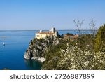 View of Duino Castle seen through blooming spring bushes along the Rilke Trail, a scenic tourist path overlooking the Gulf of Trieste, Friuli Venezia Giulia, Italy.