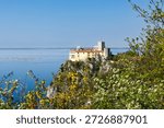 View of Duino Castle seen through blooming spring bushes along the Rilke Trail, a scenic tourist path overlooking the Gulf of Trieste, Friuli Venezia Giulia, Italy.