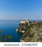 View of Duino Castle seen through blooming spring bushes along the Rilke Trail, a scenic tourist path overlooking the Gulf of Trieste, Friuli Venezia Giulia, Italy.