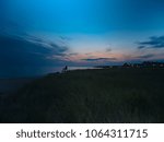 a view of the dunes of a Cape Cod beach at sunset with a lifeguard chair and the water visible in the distance 