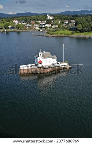 View of Dyna fyr Lighthouse built on a rocky reef and the seashore with traditional houses. Oslo Fjord near the port of Oslo, Norway vacation and travel concept