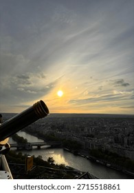 A view from the Eiffel Tower at sunset with a telescope appearing like a canon shooting the sun
