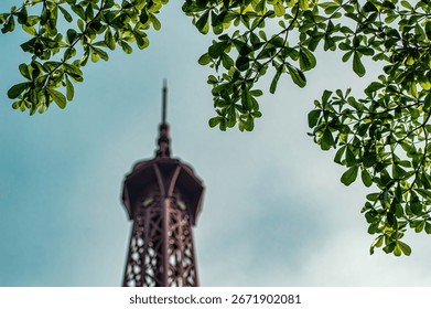 View of the eiffel tower through green tree branches against a blue sky. The iconic landmark is partially obscured by foliage, creating a natural frame and a sense of discovery.