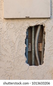 View of electrical conduit seen through a hole in the exterior stucco of a home leading to the panel box, copy space, vertical aspect