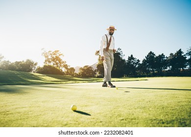 View of an elegant mature African American male golfer in a fashionable outfit with suspenders, holding a putter in his hand while walking across the golf course lit by the evening sun and thinking - Powered by Shutterstock