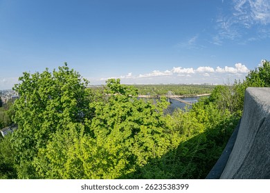 View from an elevated perspective over a well-maintained grassy area with trees, daytime lighting, distant body of water with European architectural bridges