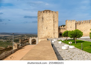 View of Elvas castle with stone walls, a tower, and a historical gate. In the foreground, a cobblestone path with green areas and benches. - Powered by Shutterstock