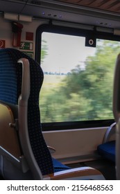 View Of Empty Comfortable And Clean Blue Seat With Sunlight Entering Through Large Window Inside A Moving German Train Wagon. No People.